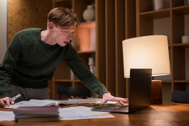 A student studying in a library with a laptop, highlighting financial planning documents and tuition payment plan brochures. The scene emphasizes focused, diligent study and preparation.