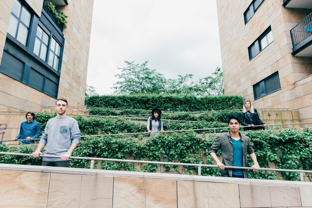 A group of diverse students standing in a circle on a community college campus, laughing and talking. The background shows a modern building with large windows and green lawns.