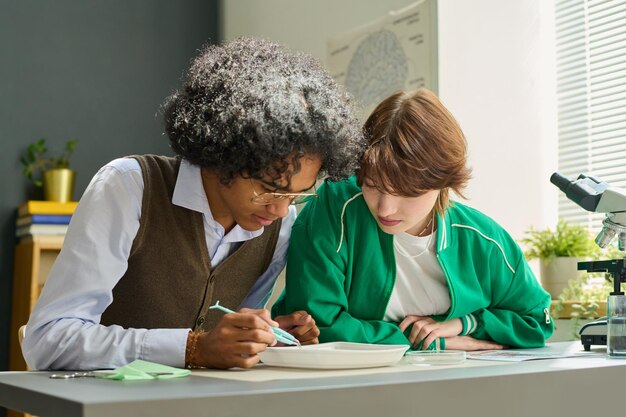 An academic advisor sitting at a desk, explaining a course catalog to a student. The advisor is pointing to a specific course, and the student is taking notes.