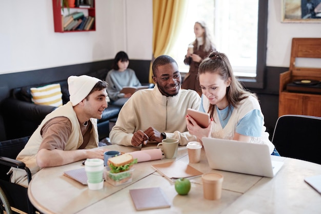 A diverse group of college students working collaboratively in a campus office, with computers and paperwork spread across a table. The image shows a sense of teamwork and active engagement.